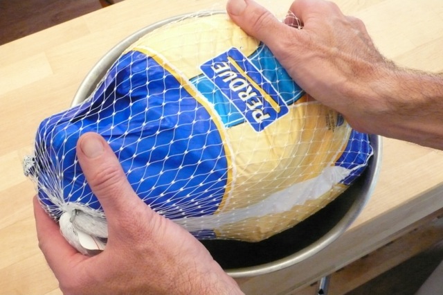 Putting a frozen turkey in a large bowl to prepare to thaw the turkey in water