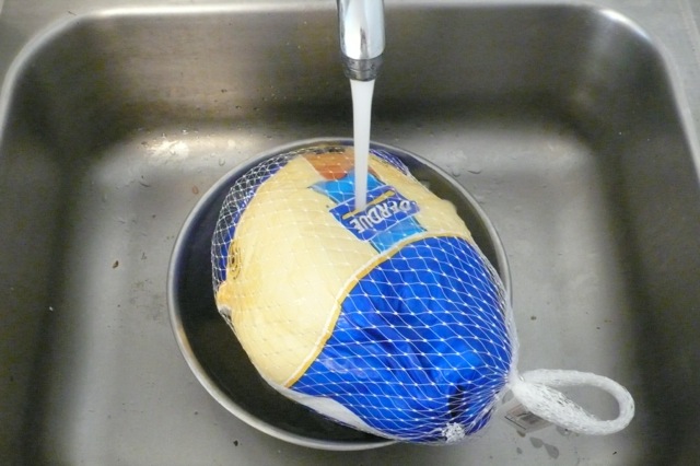 Pouring cool tap water over a frozen turkey