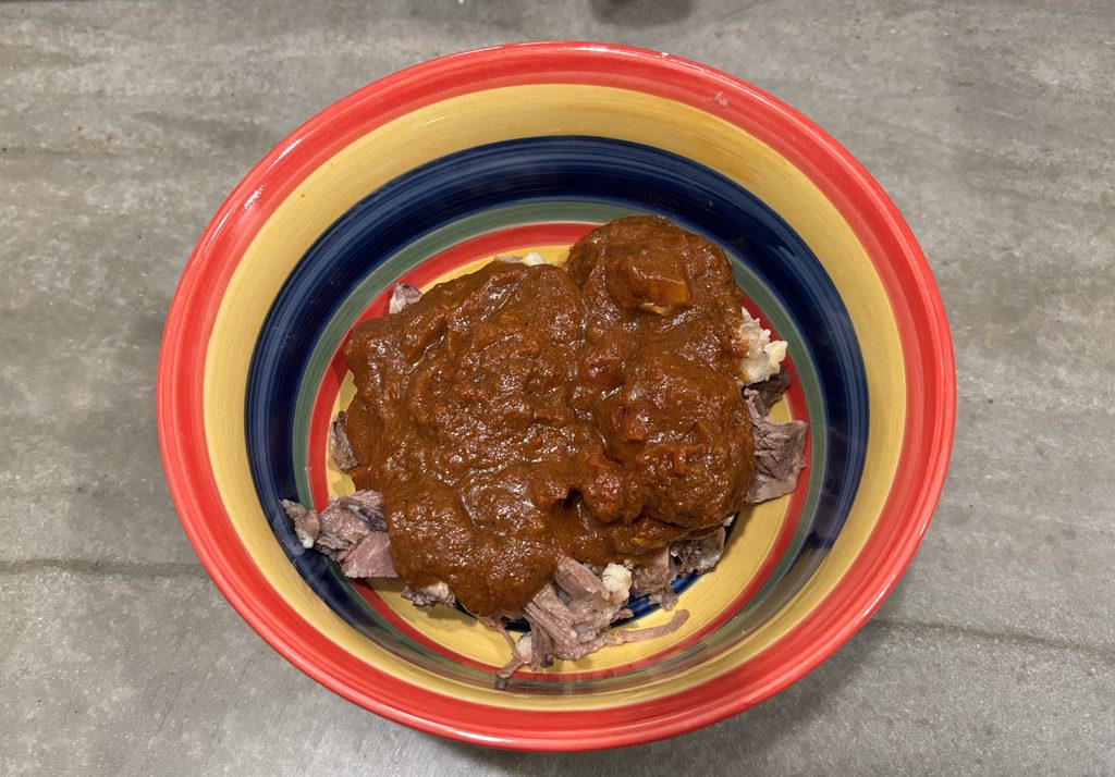 Bowl of leftover shredded beef topped with tomato sauce before microwave reheating.