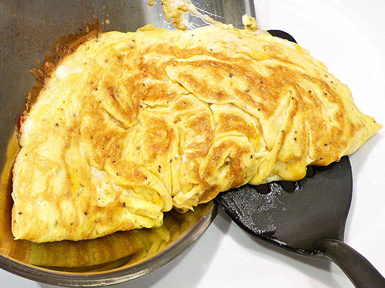 Golden cheese omelet being lifted from a frying pan with a spatula.
