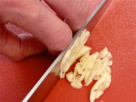 Chopping fresh garlic safely with gripping fingers curled under hand.