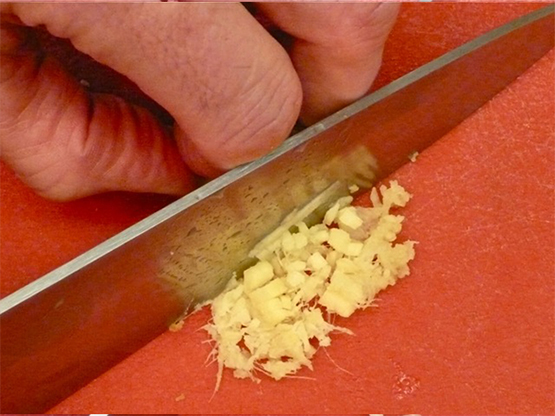 Chopping fresh ginger safely with gripping fingers curled under hand.