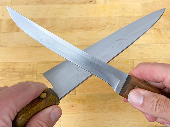 Two kitchen knives crossed together demonstrating the knife-on-knife sharpening technique.