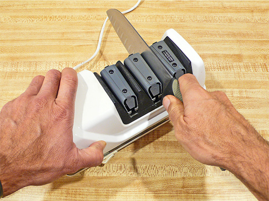 Using a multi-stage electric knife sharpener to sharpen a kitchen knife safely.